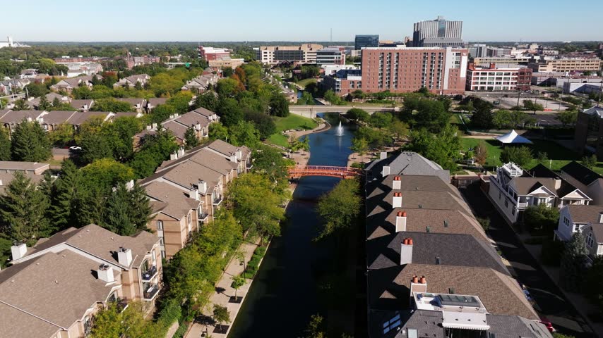 Central Canal runs between residential buildings toward a fountain and downtown Indianapolis, aerial dolly between homes