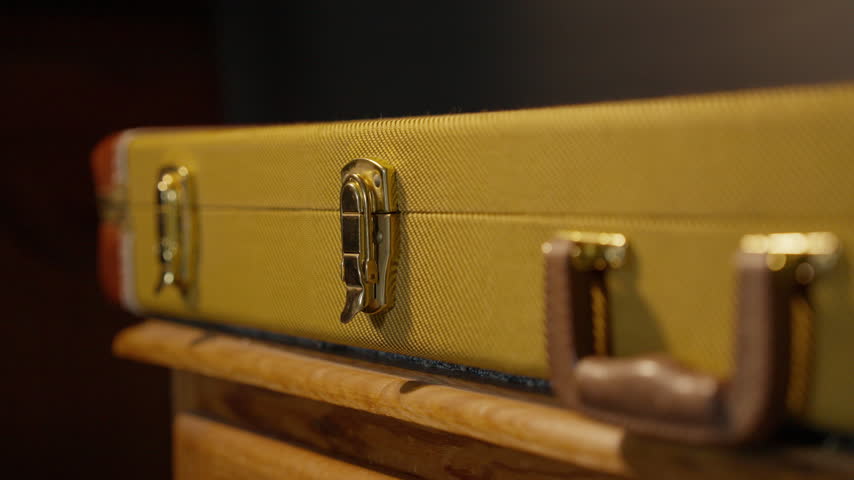 Close view of a closed tweed instrument case resting on a wooden cabinet.