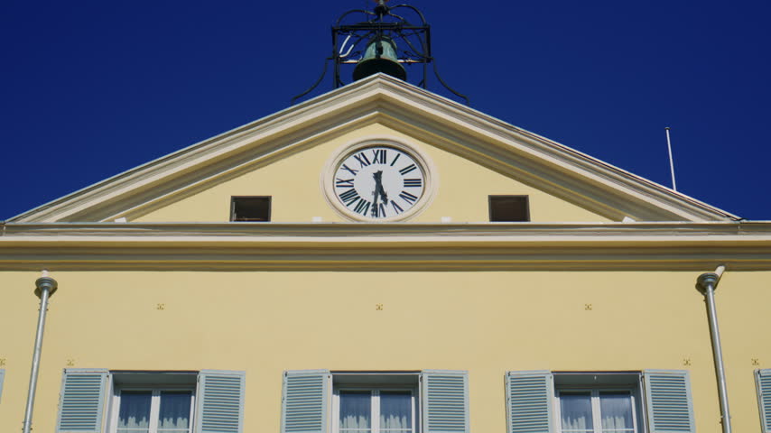 Close up of the Hotel de Ville in Antibes, featuring a pale yellow historic facade, blue shutters, Roman numeral clock, and deep blue sky, Antibes, France