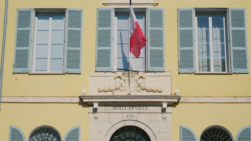 Detailed view of the Hotel de Ville, with the French flag hanging above the entrance, blue shutters, elegant stone decoration, and the "Hotel de Ville 1828" inscription, Antibes, France
