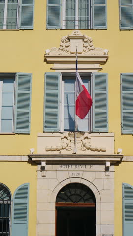Detailed view of the Hotel de Ville, with the French flag hanging above the entrance, blue shutters, elegant stone decoration, and the "Hotel de Ville 1828" inscription, Antibes, France