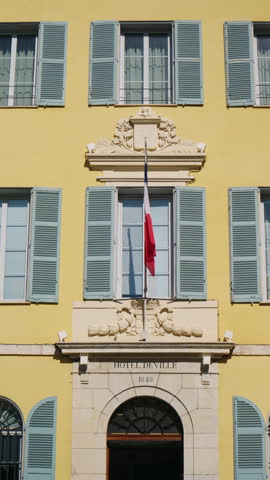 Detailed view of the Hotel de Ville, with the French flag hanging above the entrance, blue shutters, elegant stone decoration, and the "Hotel de Ville 1828" inscription, Antibes, France