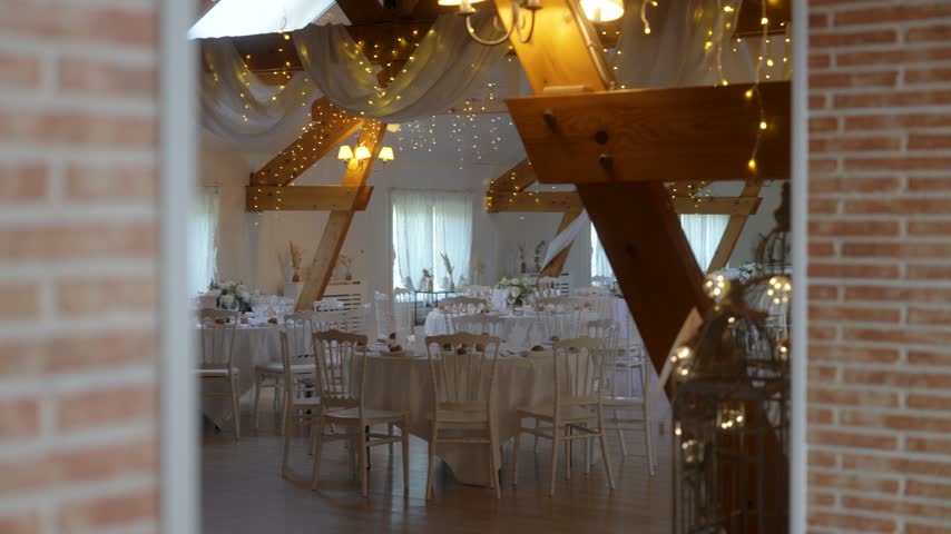 Wedding tables and chairs fill a reception hall beneath draped wooden beams.