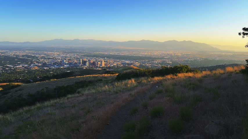 Wide shot of Salt Lake City and the valley walking on a hike on the Bonneville Shoreline Trail in Utah during golden hour on a warm spring evening, with soft light washing over the city below.