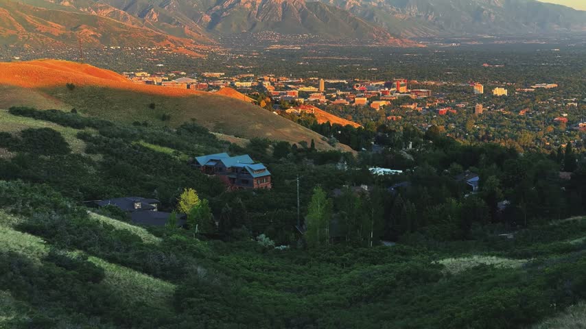 Tilting up shot of Salt Lake City and the valley from a hike on the Bonneville Shoreline Trail in Utah during golden hour on a warm spring evening, with soft light washing over the city below.
