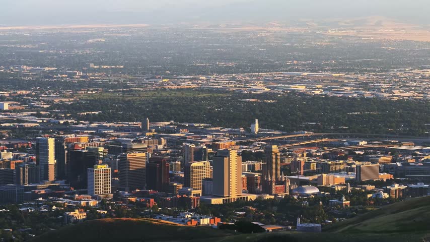 Tilting down shot of Salt Lake City and the valley from a hike on the Bonneville Shoreline Trail in Utah during golden hour on a warm spring evening, with soft light washing over the city below.