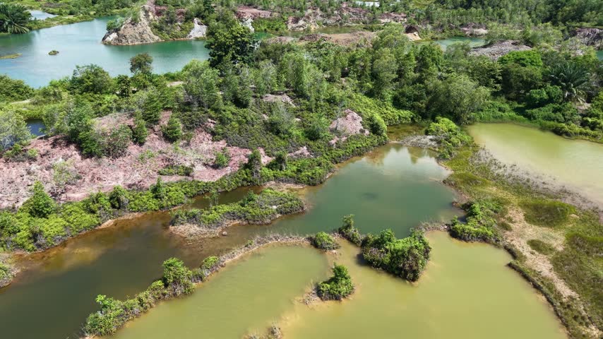 Aerial view of green water amid red rock terrain. Trees grow between rocky outcrops and pools