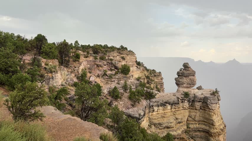 A stunning and dramatic video captured from the edge of the Grand Canyon, overlooking the vast valley in rainy weather with dense clouds swirling around the cliffs. The footage reveals misty rock formations, rain-soaked ledges, and layers of clouds rolling through the chasm, creating an atmospheric and moody scene. The raw power and scale of nature are on full display—ideal for adventure content, weather documentaries, or epic cinematic visuals.