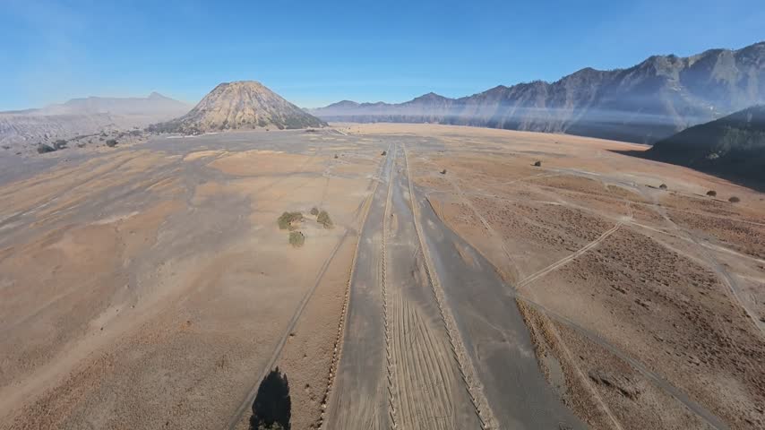 Aerial view over vast desert plains. Mountains stretch under clear blue sky