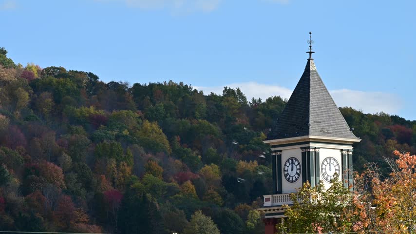 Bradford Pa valley town USA during fall season, old historic clock tower on autumn forest mountain background, time lapse video of moving clouds, trees in the wind