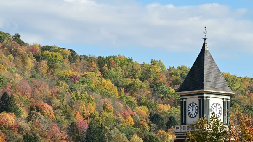 Bradford Pa valley town USA during fall season, old historic clock tower on autumn forest mountain background, time lapse video of moving clouds, trees in the wind