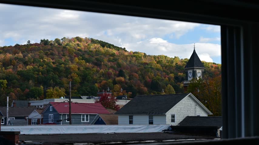 Bradford Pa valley town USA during fall season, old historic clock tower on autumn forest mountain background, time lapse video of moving clouds, trees in the wind