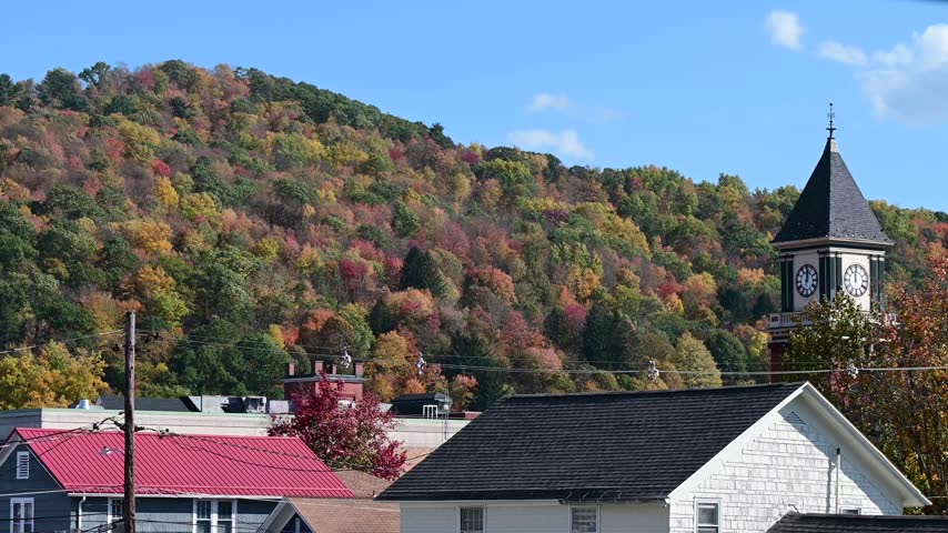 Bradford Pa valley town USA during fall season, old historic clock tower on autumn forest mountain background, time lapse video of moving clouds, trees in the wind