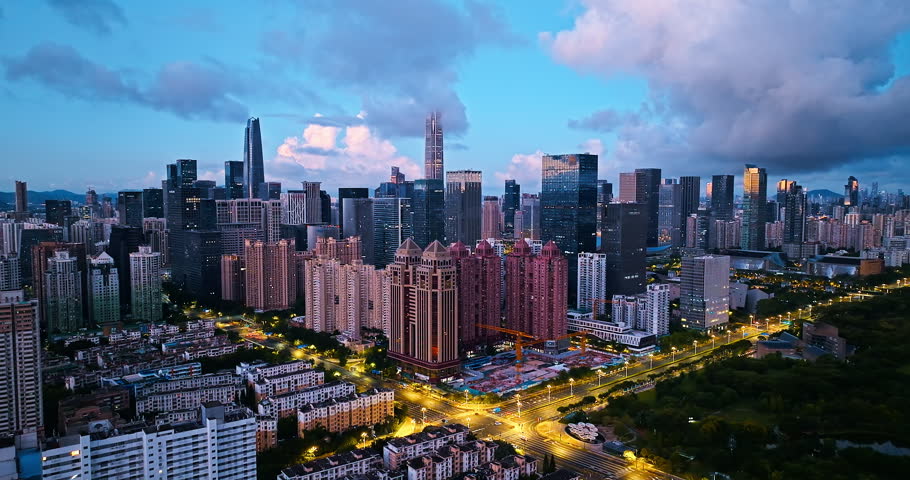 Modern modern skyscrapers illuminate the Shenzhen city skyline during dusk blue hour with glowing street traffic below.