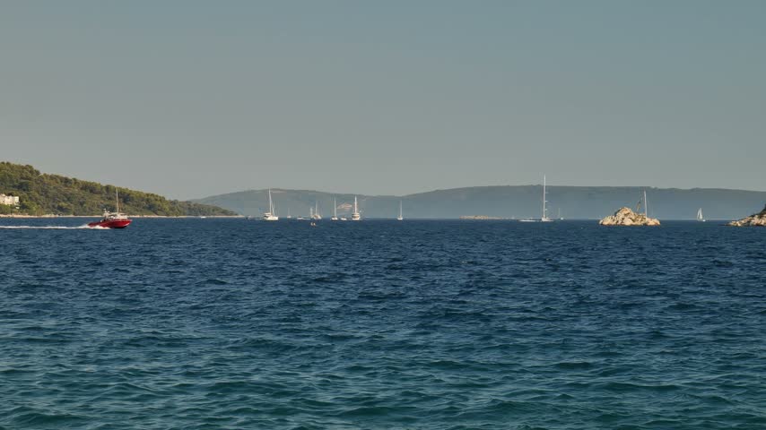 Sailboats and a red speedboat cross blue Adriatic water near Seget Vranjica and Trogir, Croatia