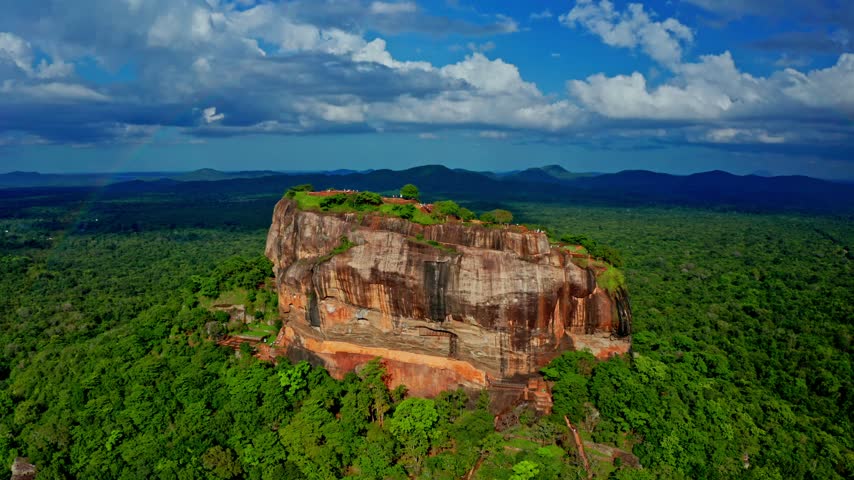Breathtaking aerial footage of ancient Sigiriya rock fortress standing majestically amidst dense tropical rainforest.