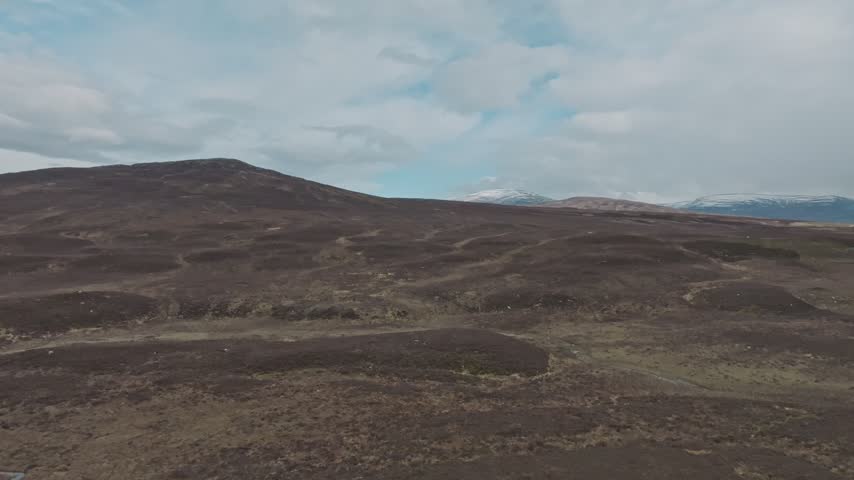 Dramatic drone perspective of desolate hills and barren landscape with snowy peaks on horizon in cloudy daylight.