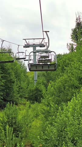 View from underneath a descending chairlift, revealing the town of Gura Humorului in the valley below surrounded by green mountain slopes.
