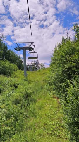 View from underneath a descending chairlift, revealing the town of Gura Humorului in the valley below surrounded by green mountain slopes.