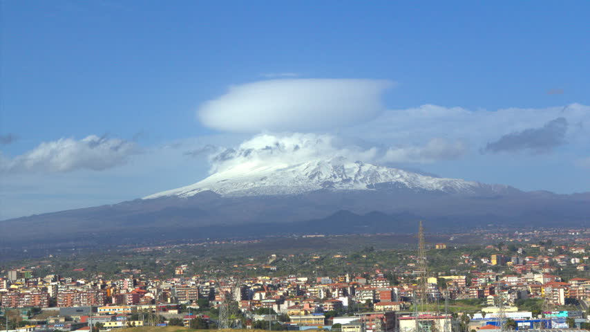 Time lapse of a lenticular cloud forming over snow capped Mount Etna with the city of Catania below on a bright clear day