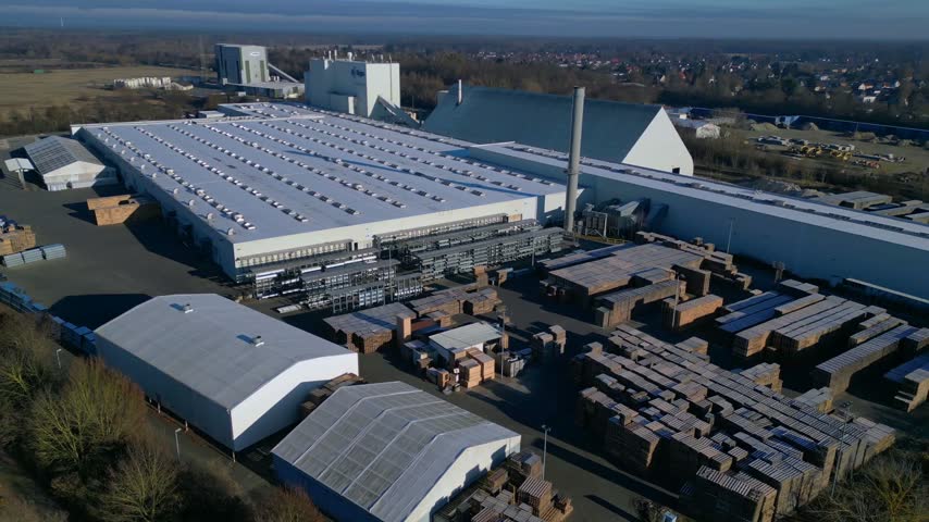 High angle aerial view of massive manufacturing plant complex featuring warehouse building and inventory of lumber stacks outdoors.