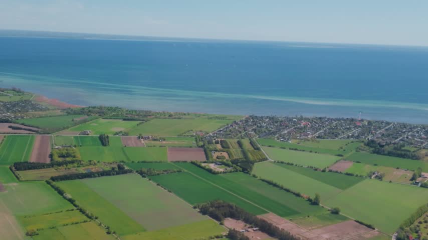 Stunning aerial perspective of Danish coastal town surrounded by lush agricultural land and clear turquoise ocean waters.