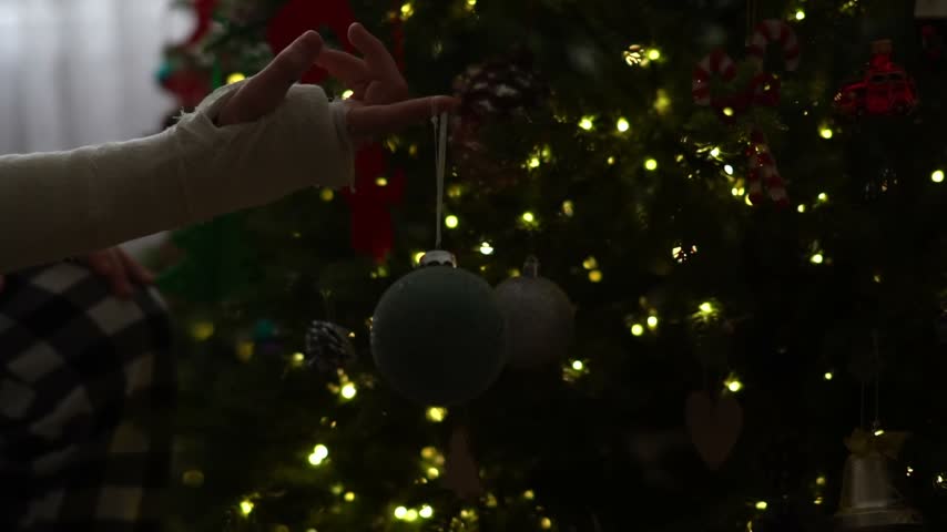 A close up of a teenagers hand in a plaster cast, holding a Christmas ornament for a Christmas or New Years tree.