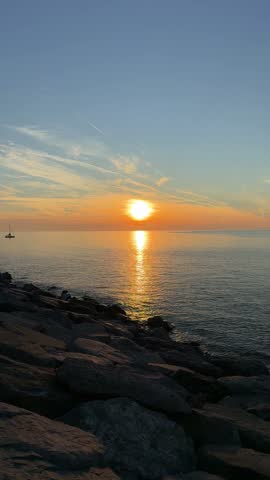 Vertical seascape photo of a rocky shoreline, bright sunset over the ocean, and a golden reflection