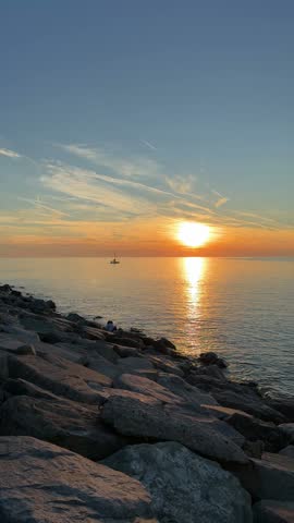 Vertical seascape photo of a rocky shoreline, bright sunset over the ocean, and a golden reflection
