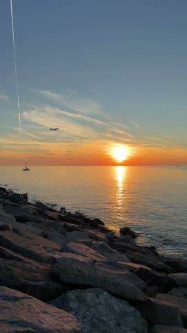 Vertical seascape photo of a rocky shoreline, bright sunset over the ocean, and a golden reflection