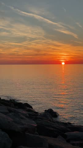 Vertical seascape photo of a rocky shoreline, bright sunset over the ocean, and a golden reflection