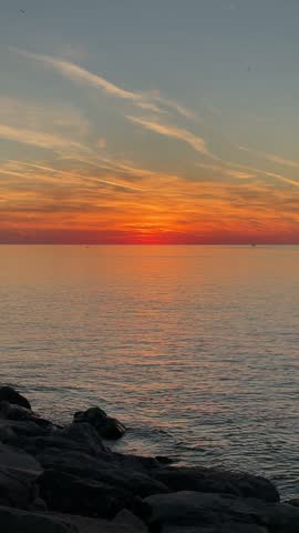 Vertical seascape photo of a rocky shoreline, bright sunset over the ocean, and a golden reflection