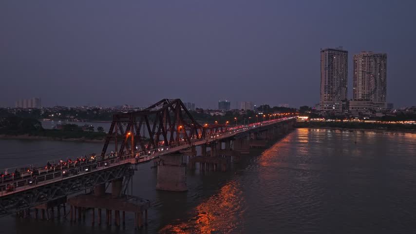 Iconic long bien bridge crossing the red river in hanoi, vietnam. Heavy traffic with motorbikes and cars moving during the evening rush hour