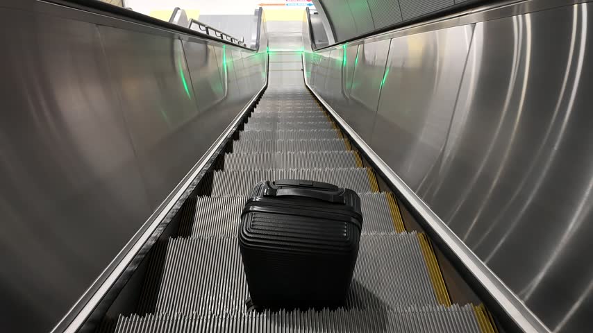 Black travel suitcase moves along a metal escalator inside a modern Istanbul metro station with stainless steel panels and green lights.