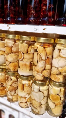 Preserved whole mushrooms are packed tightly in glass jars and displayed on a market shelf. The concept of food preservation, gourmet ingredients, and homemade delicacies is explored through this
