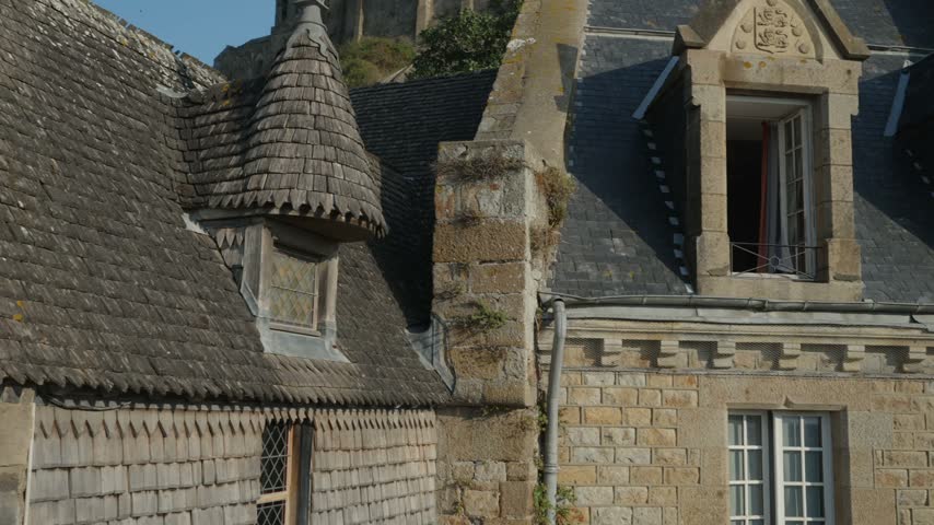 Historic stone and timber framed houses with slate roofs and tall windows at Mont Saint Michel, France, in warm sunlight