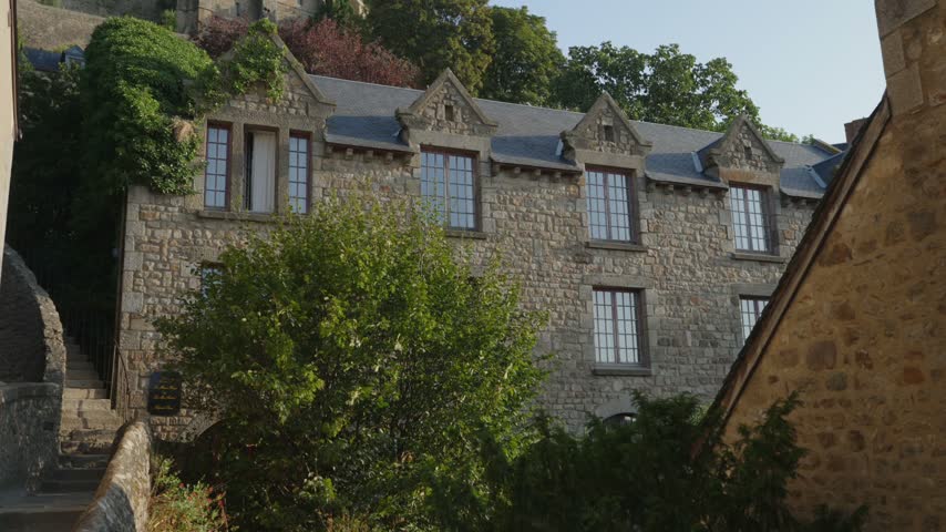 Historic stone building with Gothic windows and slate roof among green trees in Mont Saint Michel, France