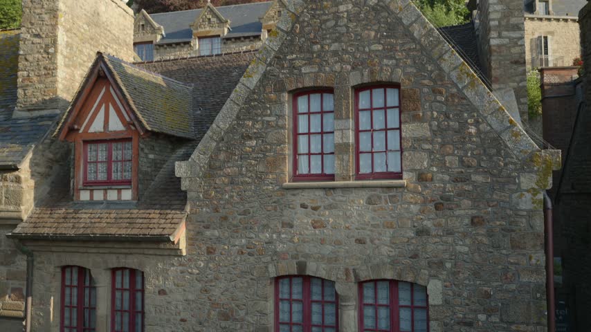Close view of medieval stone houses with steep slate roofs and distinctive red framed windows beneath Mont Saint Michel Abbey in Normandy, France