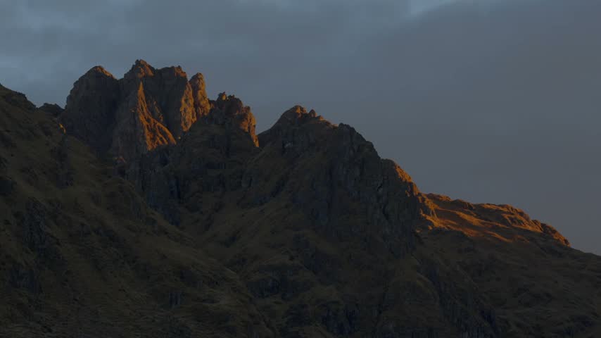 Golden alpenglow lighting up dramatic jagged Andean mountain peaks against a moody evening sky. Cinematic landscape b-roll shot in Peru.