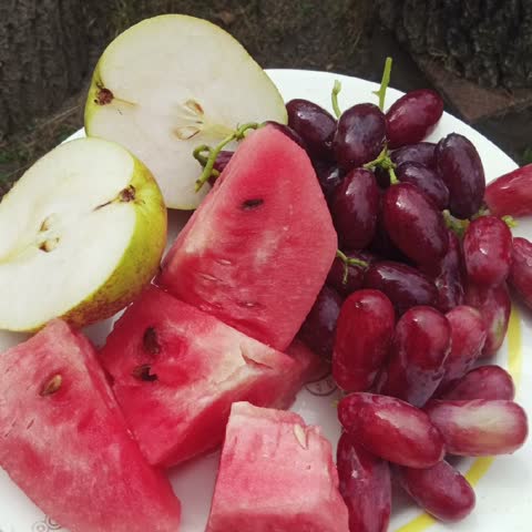 Top view of sliced watermelon, grapes and apples on a white plate, fresh fruit platter concept