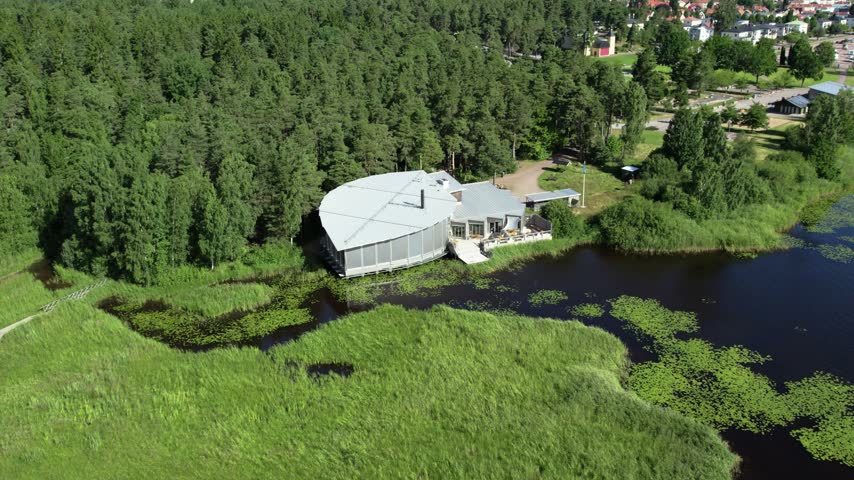 Aerial drone view of Naturum Varmland surrounded by green fields trees and a dark pond with wetland areas near Marieberg in Karlstad Sweden.