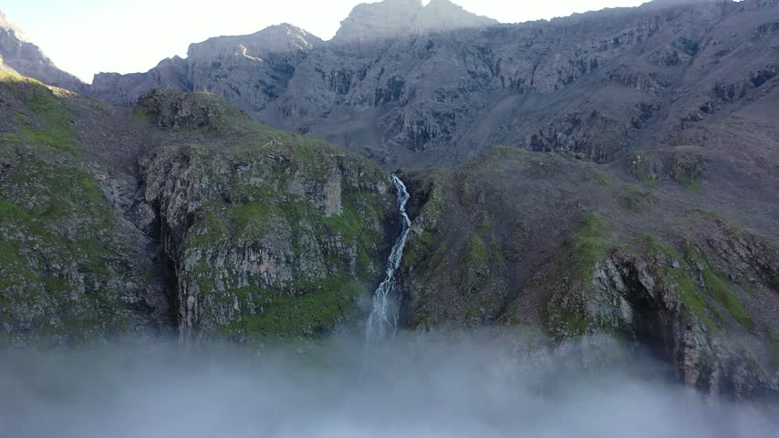 Aerial drone footage of Xijisiduo Waterfall in Mengtun River Valley, Aba, Sichuan, China, as water cascades down mossy rocky cliffs and disappears into a thick sea of clouds.