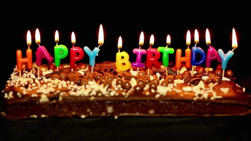 Chocolate birthday cake decorated with multicolored candles spelling Happy Birthday, capturing a cheerful celebration with colorful lights and festive dessert details.