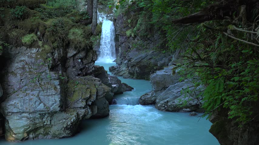 Mamquam Falls on the turquoise Mamquam River in Squamish, British Columbia. Glacial water flows through a rugged stone canyon surrounded by dense forests during a summer day.