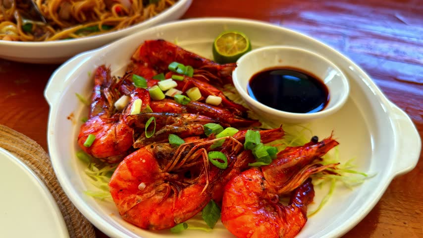 A plate of fried shrimp drizzled with lime juice and a delicious sauce in a small bowl.