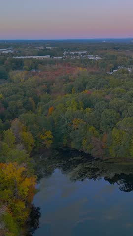Scenic autumn landscape at Stanley Quarter Park in Connecticut, USA, featuring vibrant fall foliage, colorful trees reflected in calm water, and soft evening light. Vertical.