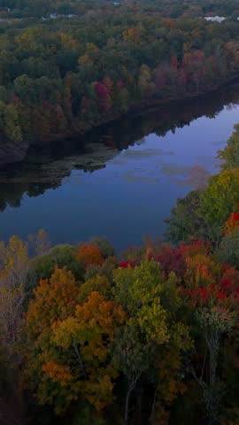 Aerial view of Stanley Quarter Park in New Britain, Connecticut, USA, featuring a calm lake reflecting the sunset sky amid colorful autumn foliage. 4K. Vertical.