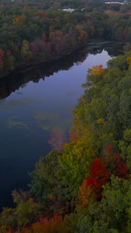 Aerial view of Stanley Quarter Park in New Britain, Connecticut, USA, featuring a calm lake reflecting the sunset sky amid colorful autumn foliage. Vertical.