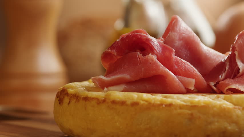Spanish omelette with jamon serrano, tortilla and iberico cured ham appetizer on wooden table, traditional Spanish breakfast close up in cafe