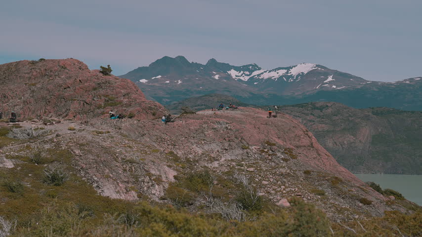 Hikers Resting on Rocky Ridge Overlooking Mountains and Lake Grey in Torres del Paine, Patagonia, Chile